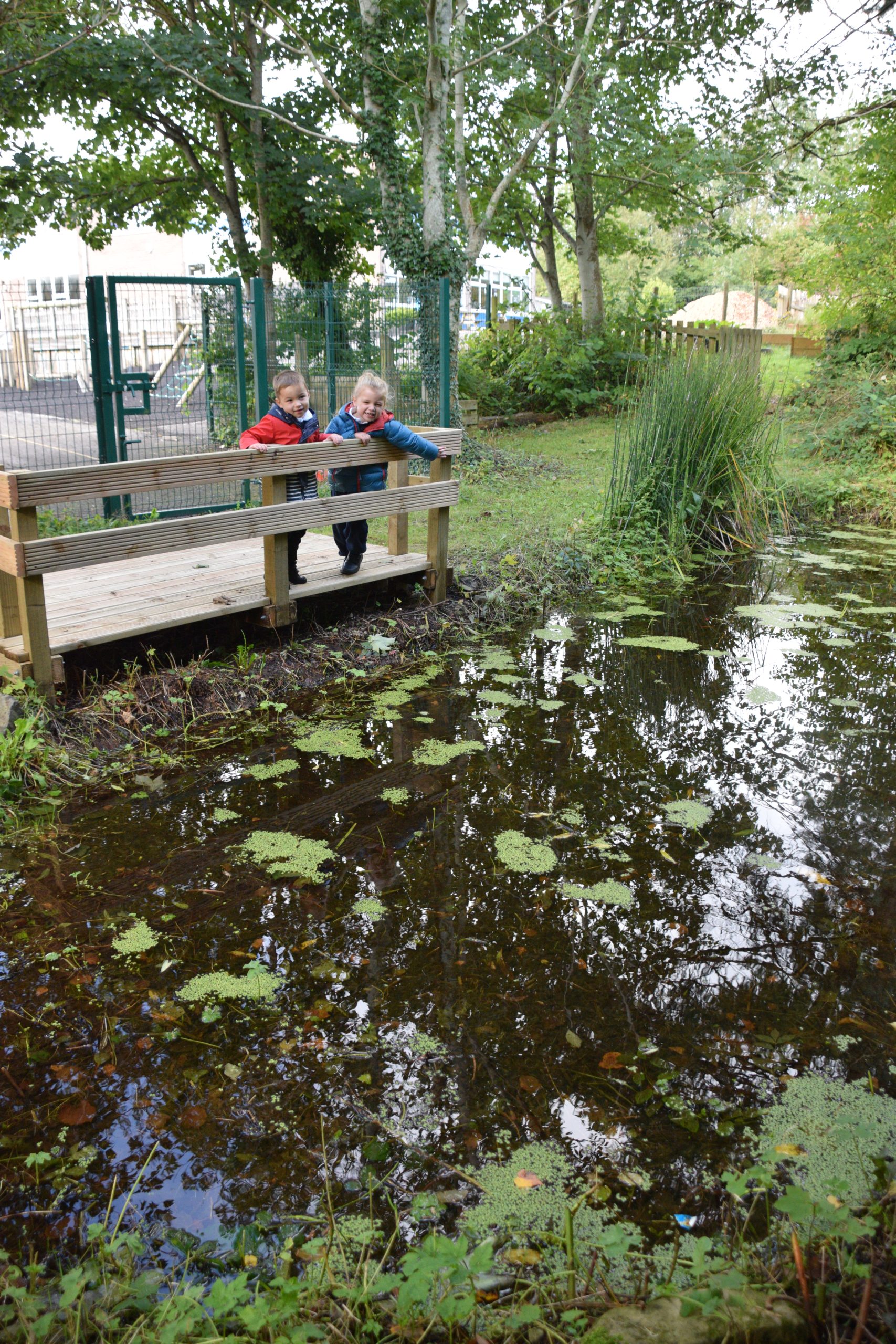 Nursery children exploring the outdoor area beside a pond